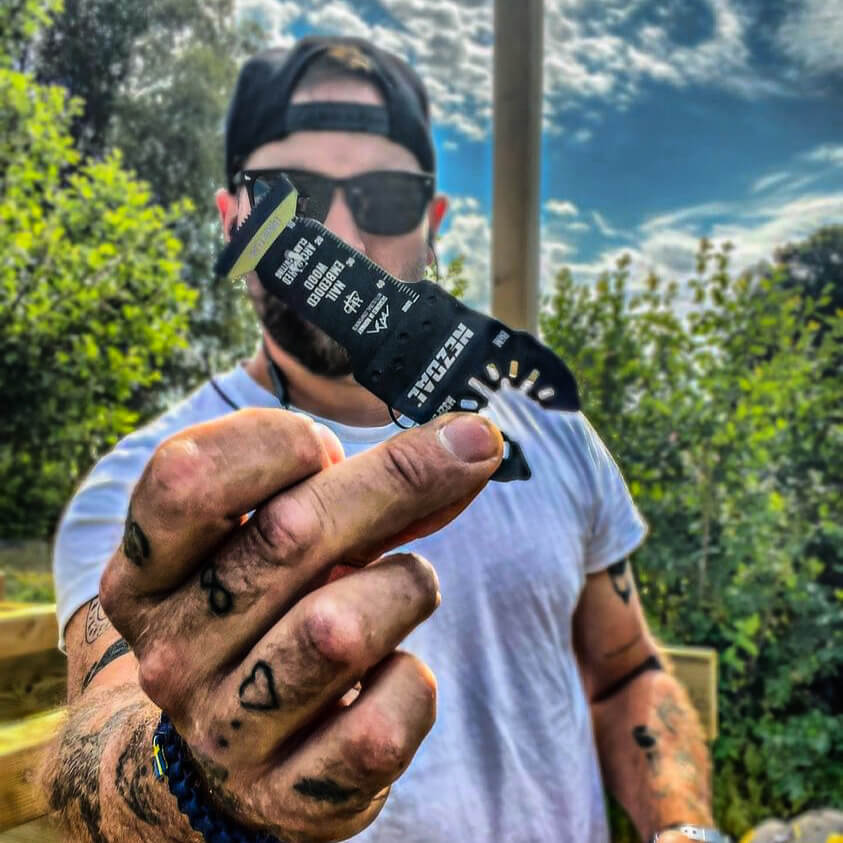 carpenter with tattoos holding a oscillating multi-tool blade in his hand